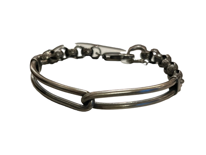 A dark gunmetal silver double-band bracelet with a central knot detail and a lobster clasp, resting on a textured light gray surface.